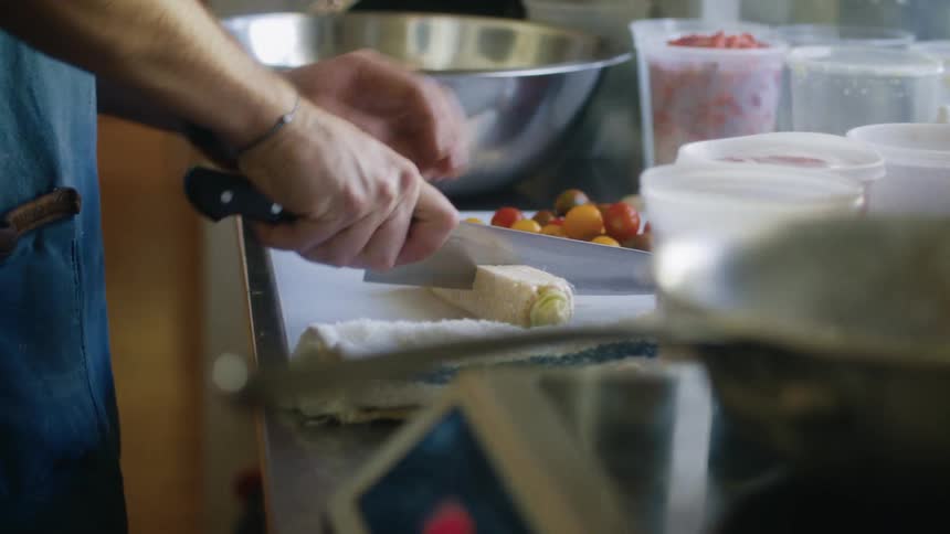 A person slices corn on a kitchen counter surrounded by fresh ingredients
