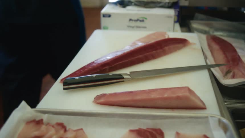 Sliced raw fish sits on a cutting board with a knife beside it