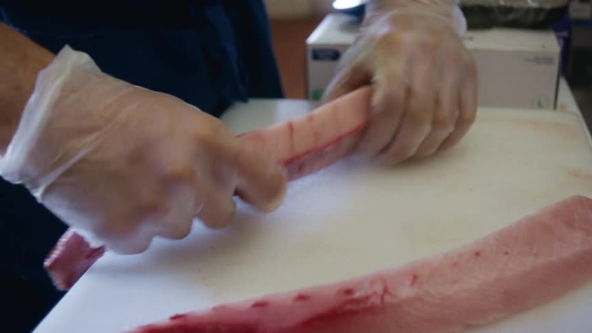A person wearing gloves is handling raw fish fillets on a cutting board in a kitchen