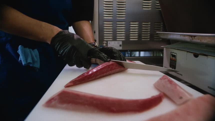 A chef slices raw fish fillets on a cutting board in a commercial kitchen