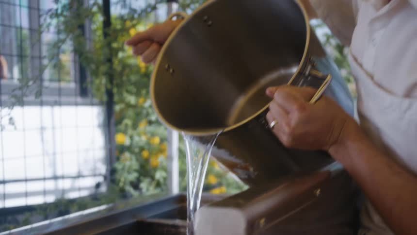 The cook pours water from a pot under a tent
