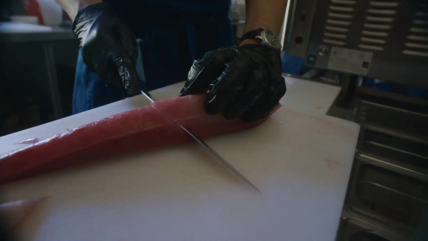 Hands with gloves and a knife cutting a salmon