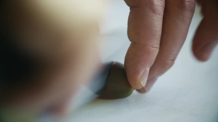 Closeup of a person slicing a small fruit or vegetable with a knife
