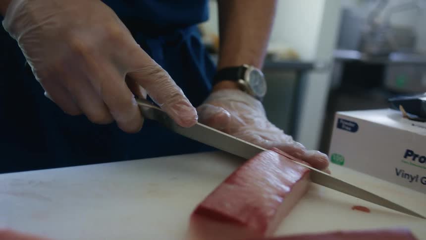 Close up of a male chef cutting meat into thin slices on a counter top in a kitchen during daytime