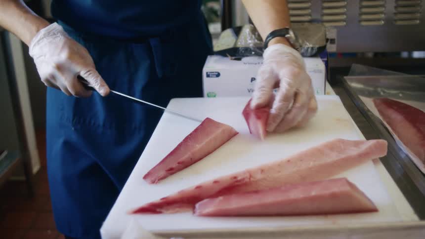 A person slices raw fish fillets on a cutting board in a commercial kitchen