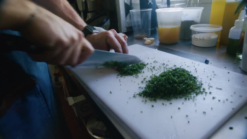A male chopping up greens in a kitchen
