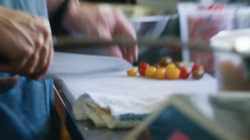 A man is cutting tomatoes with a large knife in a kitchen