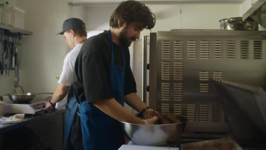 Two men in a restaurant kitchen with aprons cooking