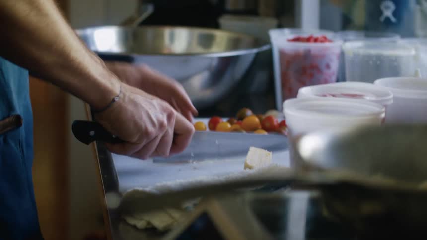 A kitchen workspace is prepared for cooking with a cutting board holding colorful cherry tomatoes various containers of ingredients nearby