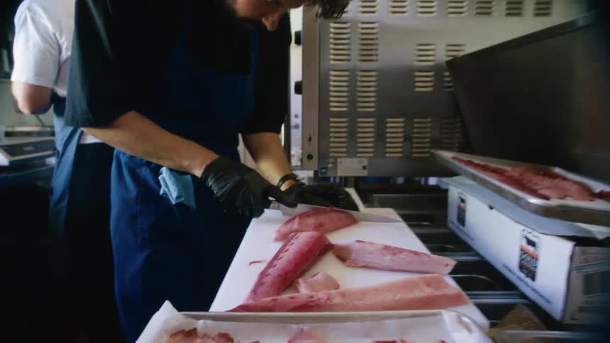A chef slices thick pieces of raw fish on a white cutting board in a kitchen