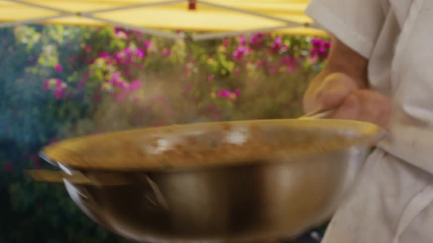 Cook tosses food in pan under yellow canopy