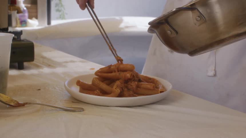 A chef plates pasta from a pan onto a dish using tongs