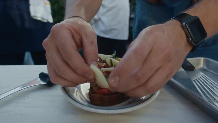The cook is plating the food on the counter outside