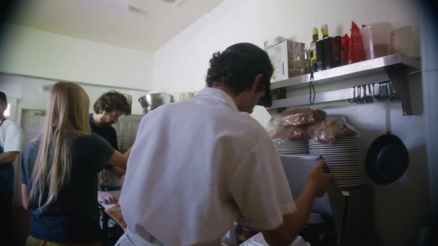A man walks into a restaurant kitchen revealing others inside cooking and preparing meals