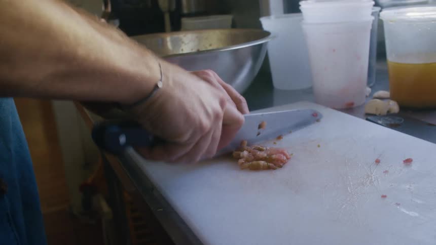 Person finely chops shrimp on a cutting board in a kitchen setting