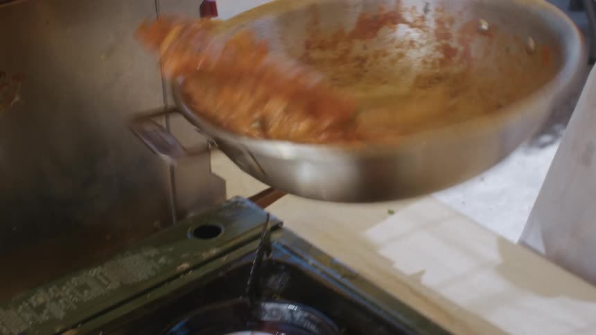 Person stirring a pan of pasta and sauce