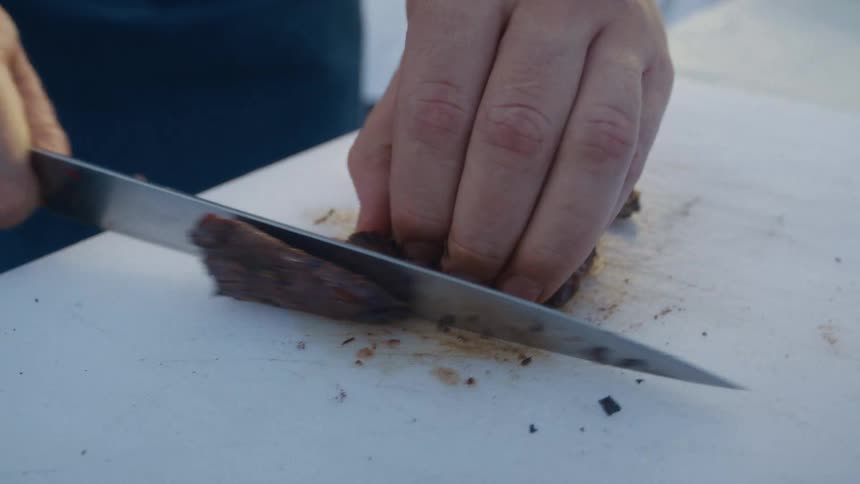 Pair of hands with a knife cutting a slice of meat