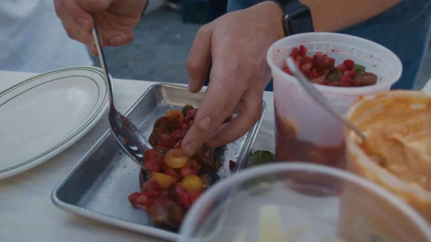 Pair of hands with a spoon seasoning meat on a baking sheet