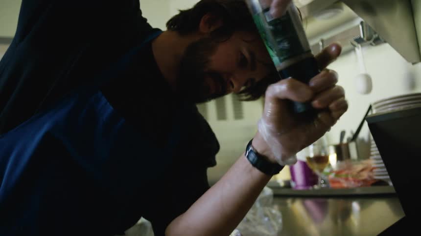 A chef squeezes sauce onto food in a kitchen setting