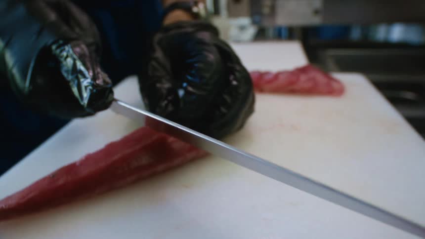A chef wearing gloves slices steaks on a white table