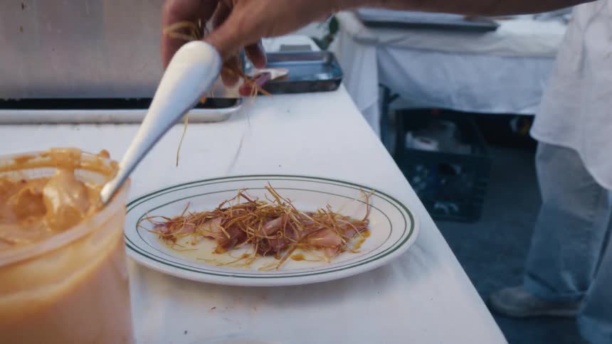 A chef hand plates a delicate garnish on a dish at a food preparation station