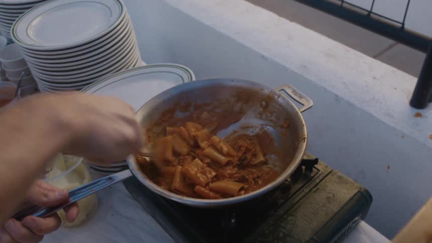 Person preparing pasta with sauce in a frying pan