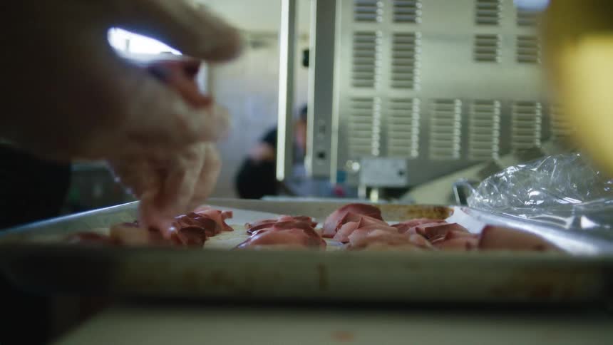 Pair of gloved hands separating small pieces of meat on a baking sheet