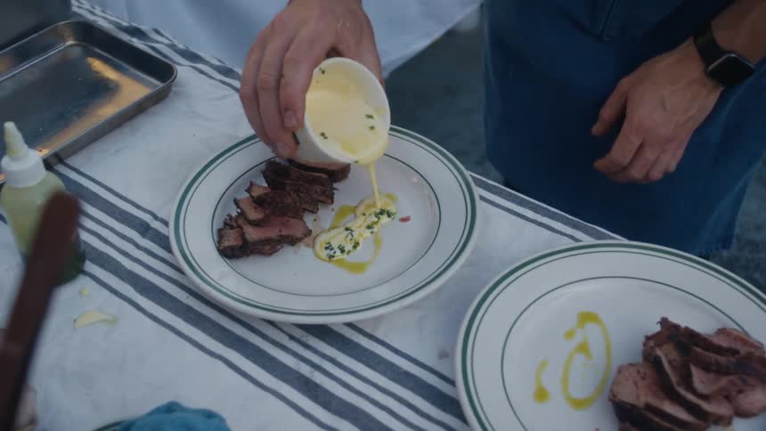 A person pouring cream on a plate of stake