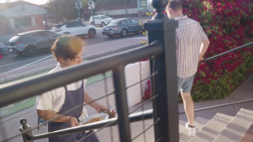 Man in apron walking through a restaurant with two plates