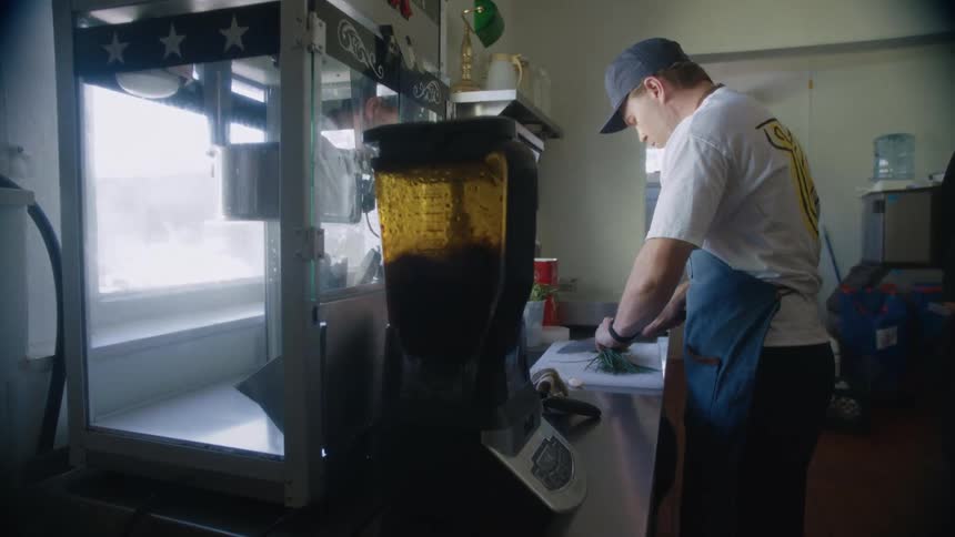Blender in operation and next to it a man in a cap chopping parsley
