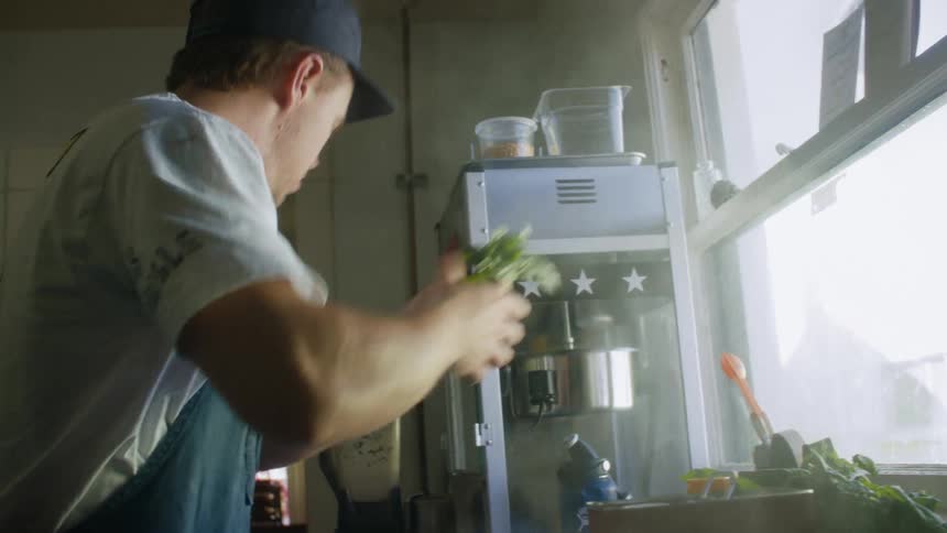 A man is cooking in the kitchen by the window