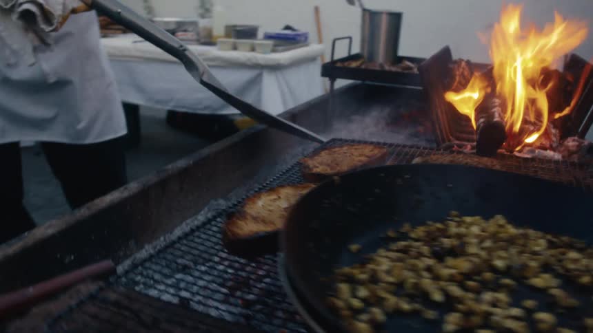Person adjusts flaming logs on outdoor grill with food cooking