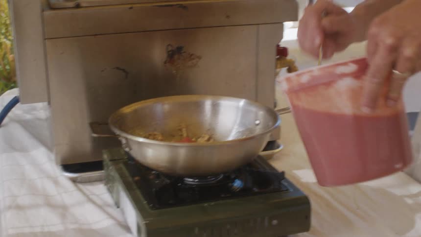 A man spoons sauce into the pan on the burner
