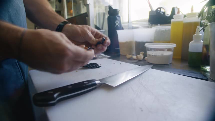 Person opens dried chili to release seeds onto a cutting board in a kitchen