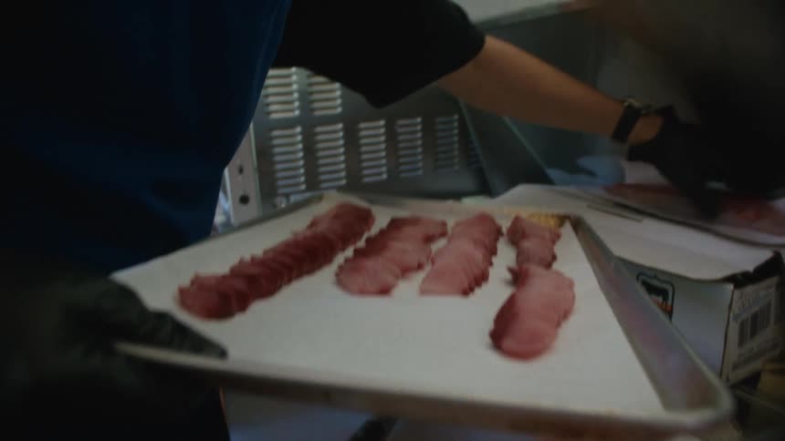 The man is slicing meat in the kitchen