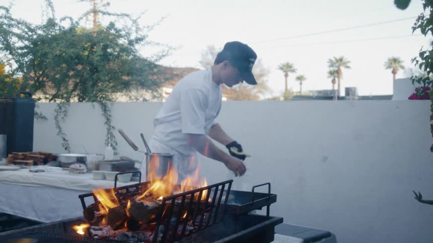 A man adds wood to the outdoor grill