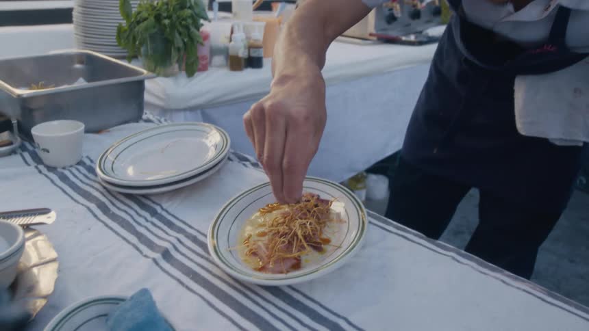 Chef in black apron finishing a dish with seasoning