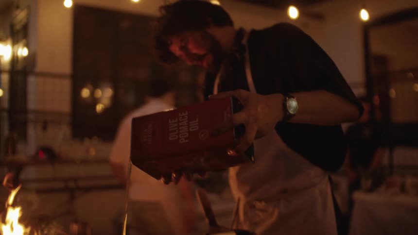Man in a kitchen at night in an outdoor area putting oil