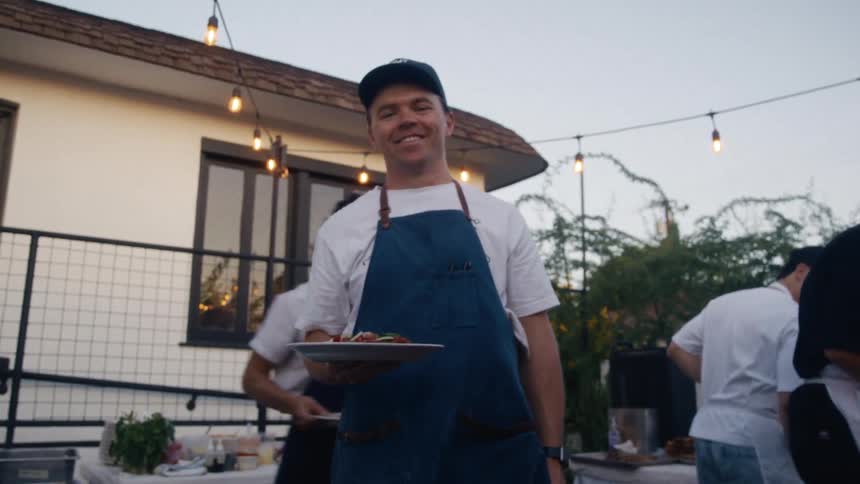 Men in an outdoor kitchen with one of them looking happy holding a cooked dish