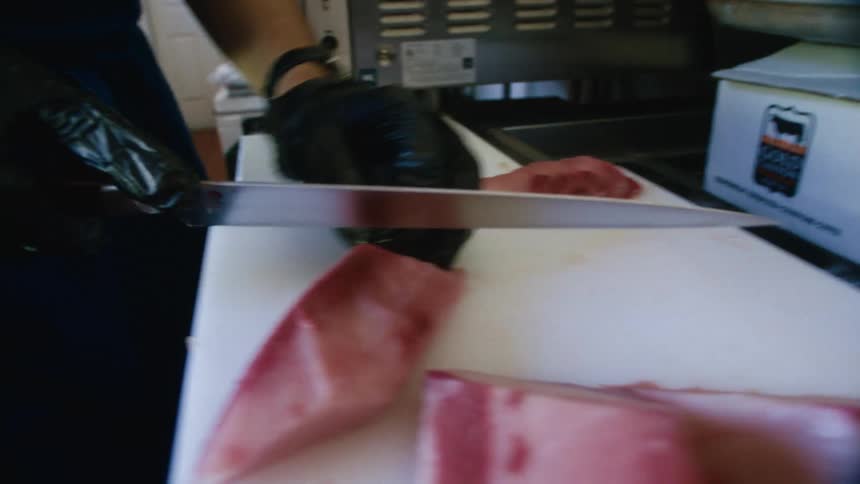 Close up of a male chef cutting meat into thin slices on a kitchen counter top