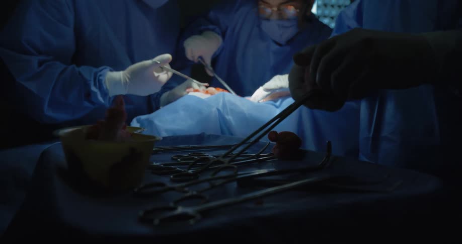 Close up of a surgery assistant helping surgeons with gauze and surgical instruments as they perform a surgery in an operating theatre