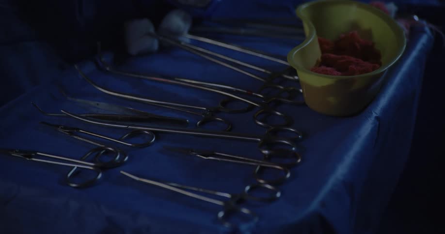 Gloved hand handling scalpel on a table with blood stains