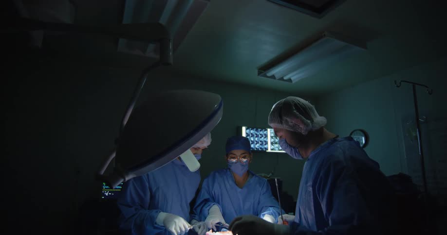 Group of surgeons perform a surgery in a theatre under theatre lights