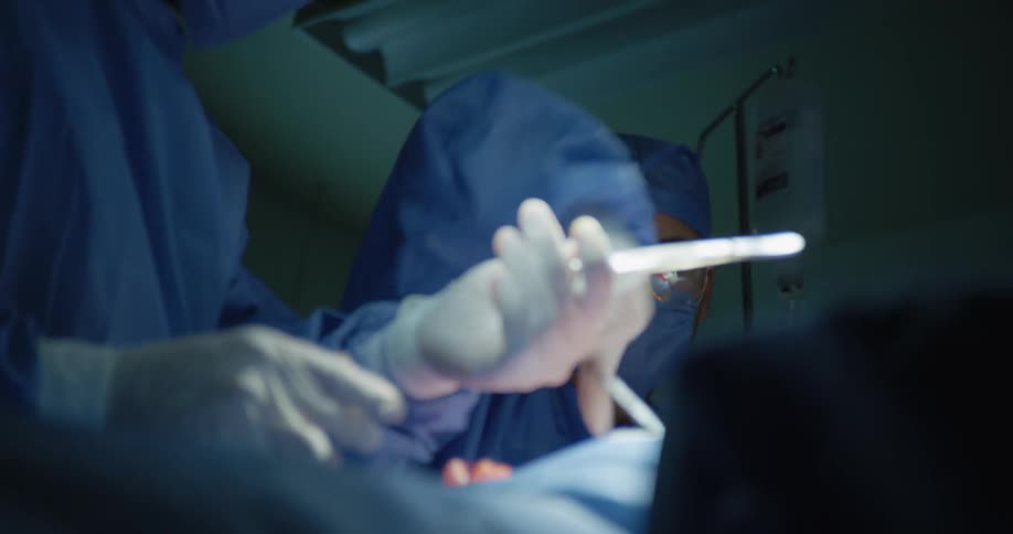 Woman with other colleagues performing surgery and using scalpel