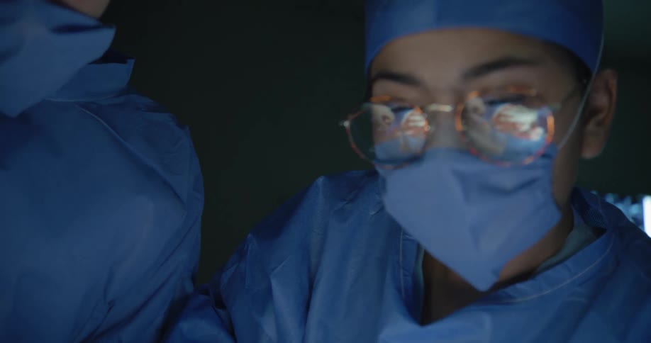 Close up of two surgeons performing a surgery in an operating theatre under theatre lights