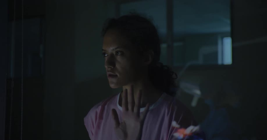 Female patient in pink outfit putting her hand on the glass and watching a surgical procedure