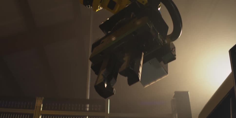 A robotic arm is positioned under dramatic lighting in an industrial or manufacturing setting casting shadows against the ceiling