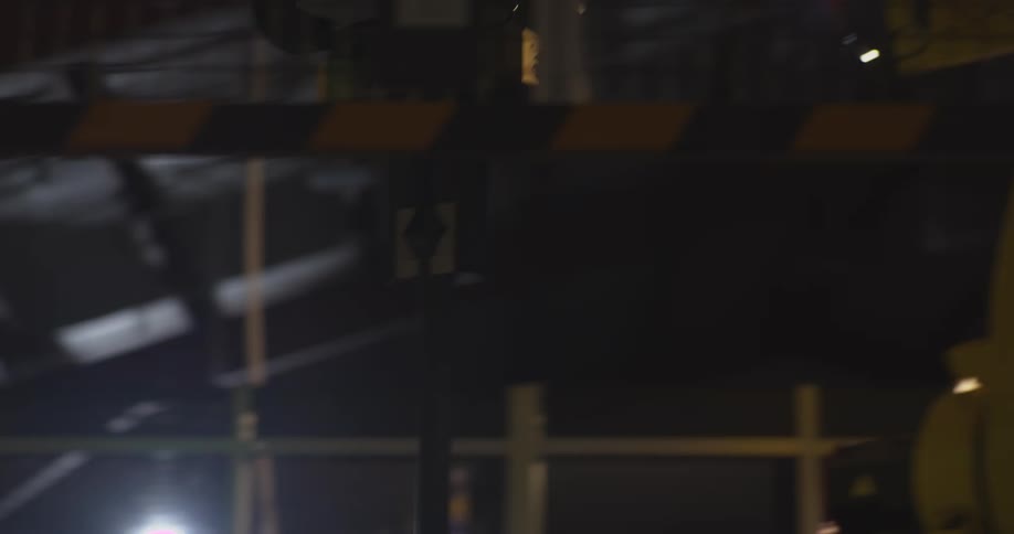 A yellow robotic arm operates in a dimly lit industrial setting partially illuminated by bright overhead lights