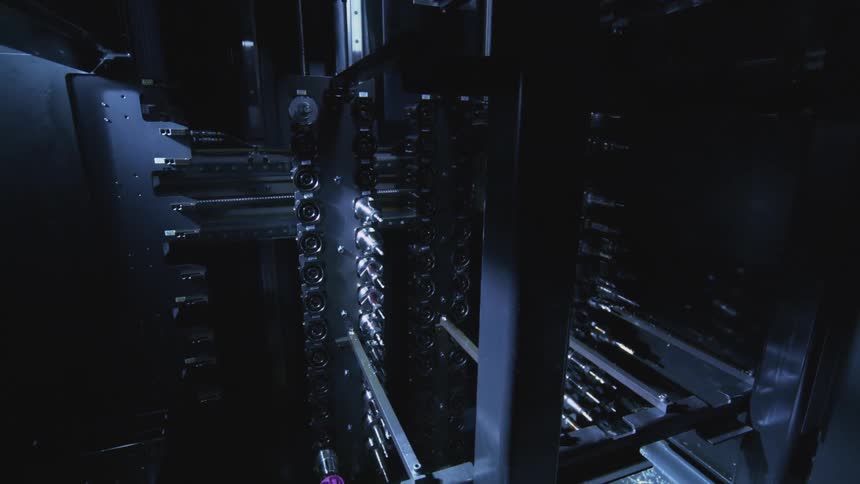 Metal components are stacked inside a dark hightech manufacturing machine illuminated by cool blue lighting