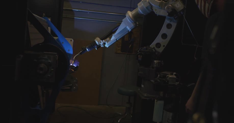 Person in a factory watching a robotic arm welding an object